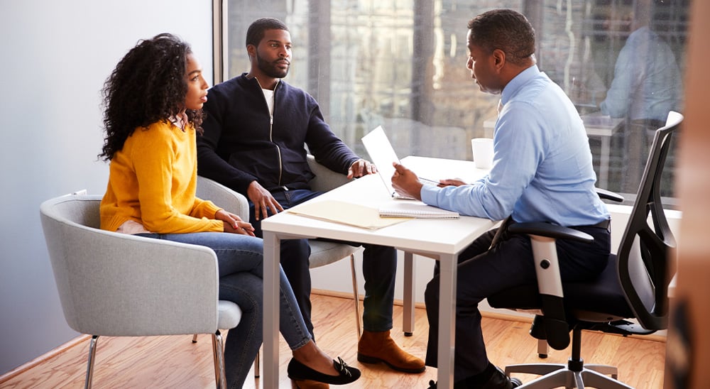 A male lender meeting with a couple in his office They are reviewing refinancing mortgage docu