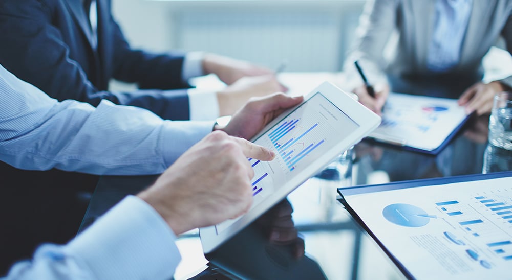 Lenders meeting at a boardroom table and reviewing data on tablets