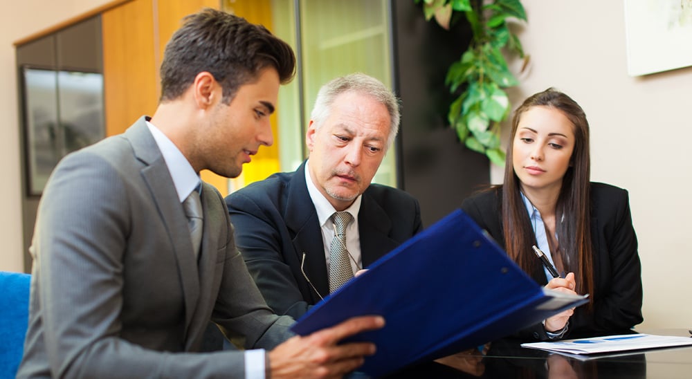 Three lenders reviewing mortgage documents at a boardroom table