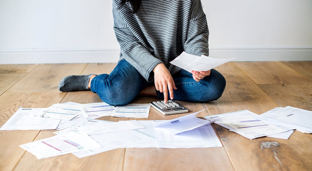 Person sitting on the floor with a calculator and surrounded by papers