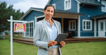 a real estate professional stands in front of a just-sold house, holding a tablet device in her hands