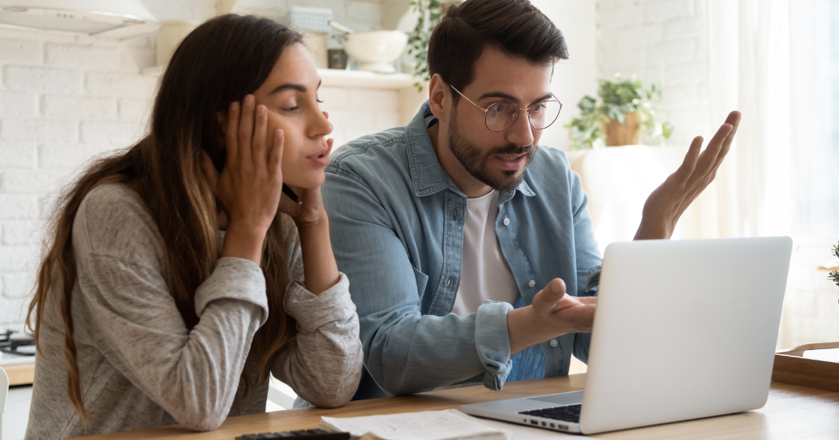 A couple considers troubling information on their laptop screen, in their kitchen.